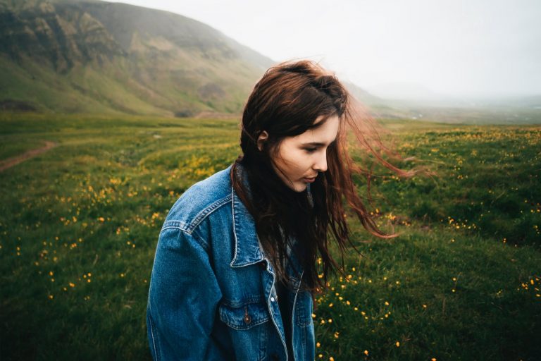 woman wearing blue denim jacket walking on the green grass field